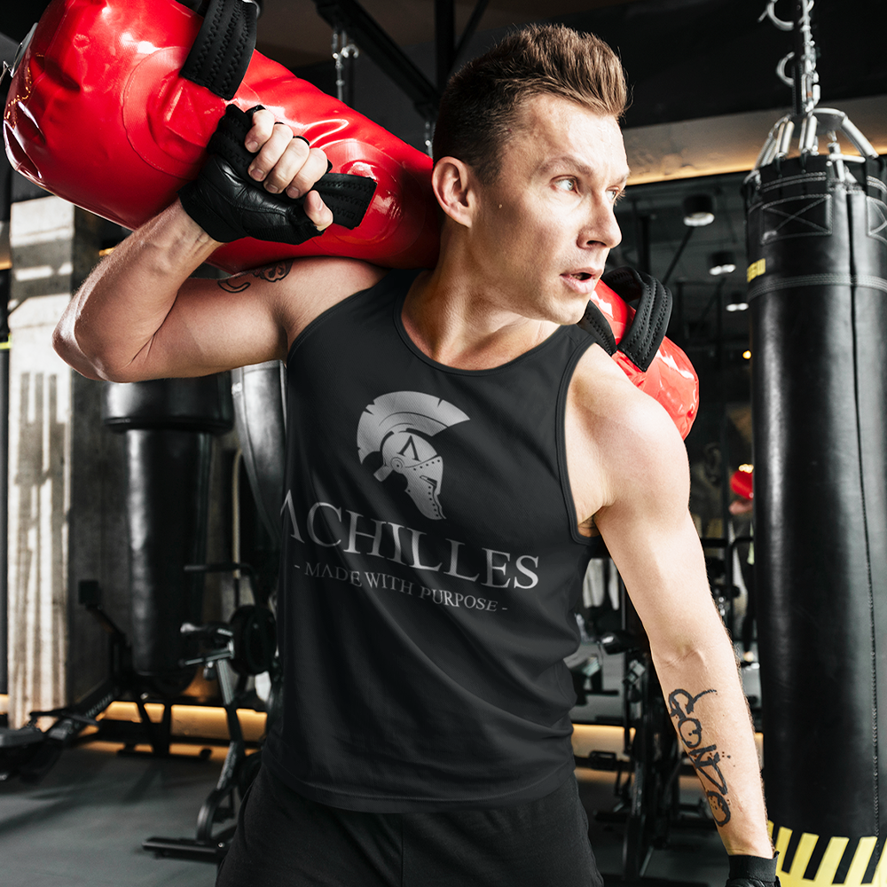 Front view of a fit man carrying a weighted training bag wearing a black training tank vest top in the gym with grey Achilles logo printed across the front