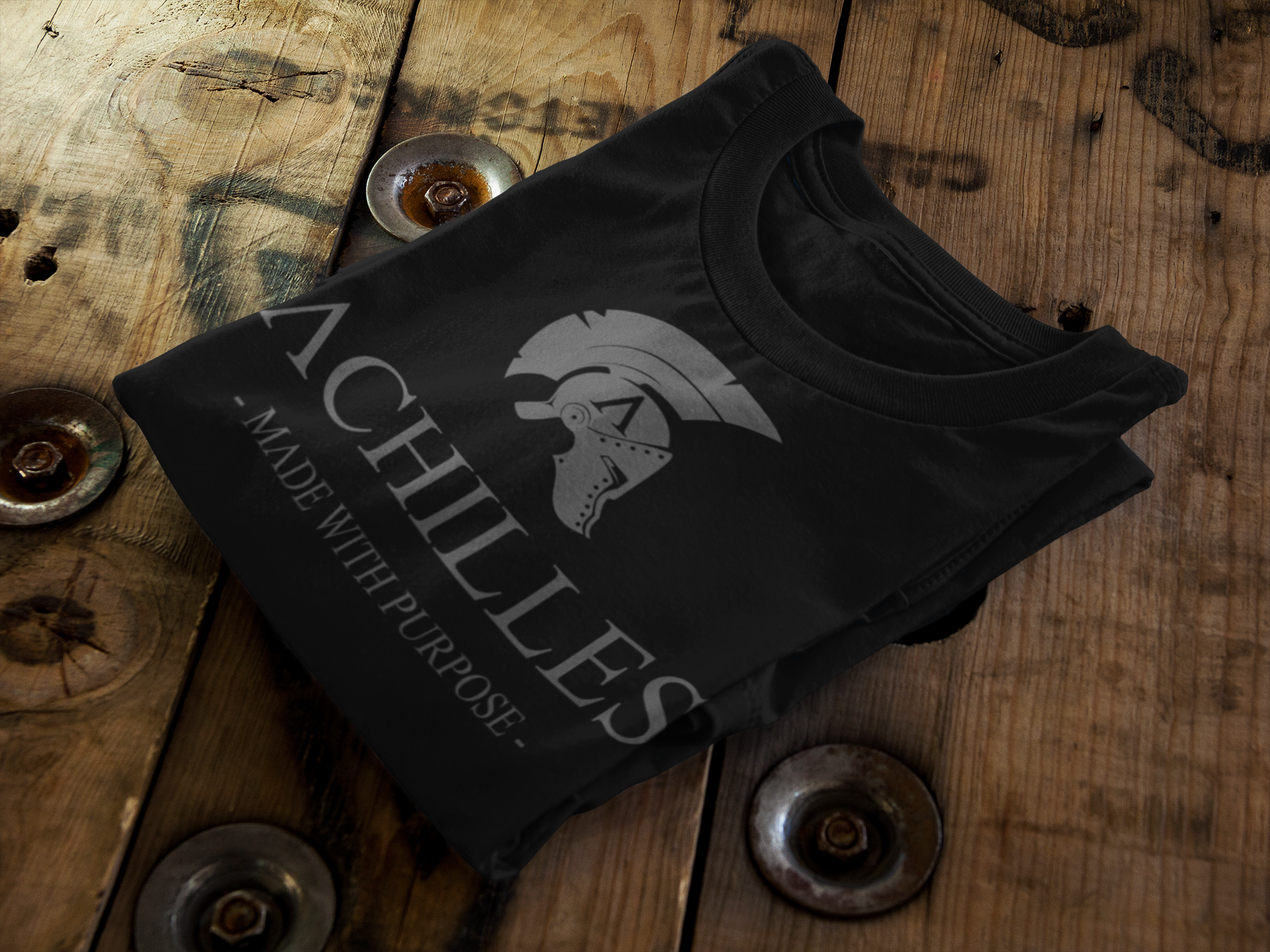 Folded black cotton T-shirt on a wooden table by Achilles Tactical Clothing Brand with the Achilles logo printed in grey across the front